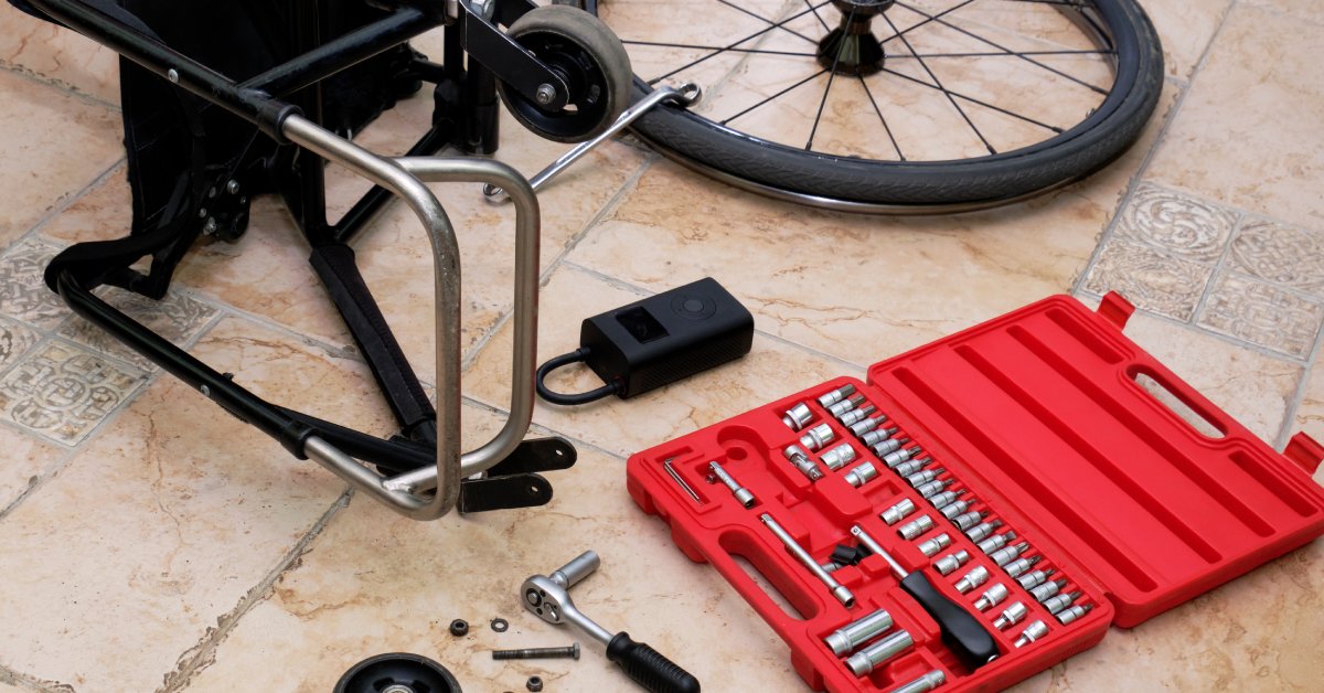 A black manual wheelchair lies on its side next to a red socket wrench kit for repairing the front caster wheel on the floor.