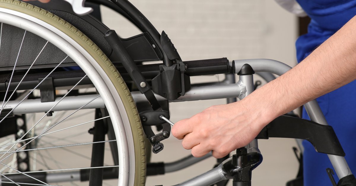 A person is using a tool to adjust a bolt on a wheelchair lock. They are holding a wrench in their right hand.