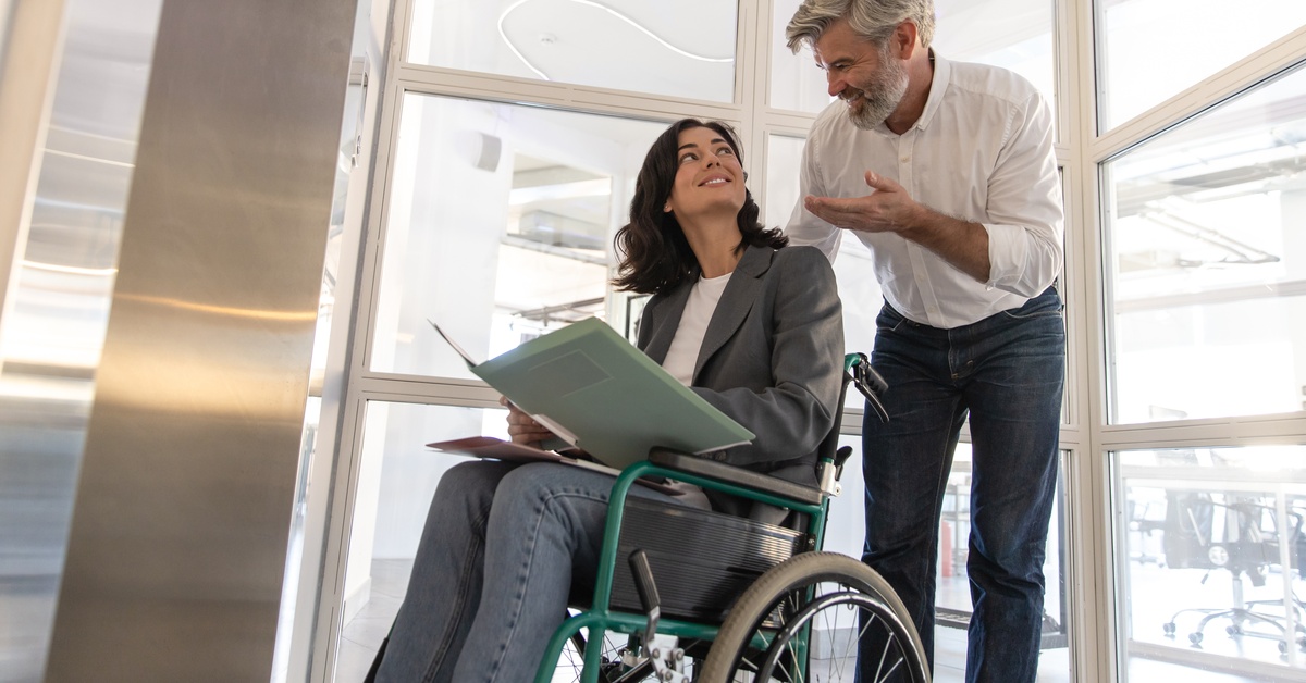 A man discussing something with a woman in a wheelchair. The woman has files in her lap as she looks at the man.