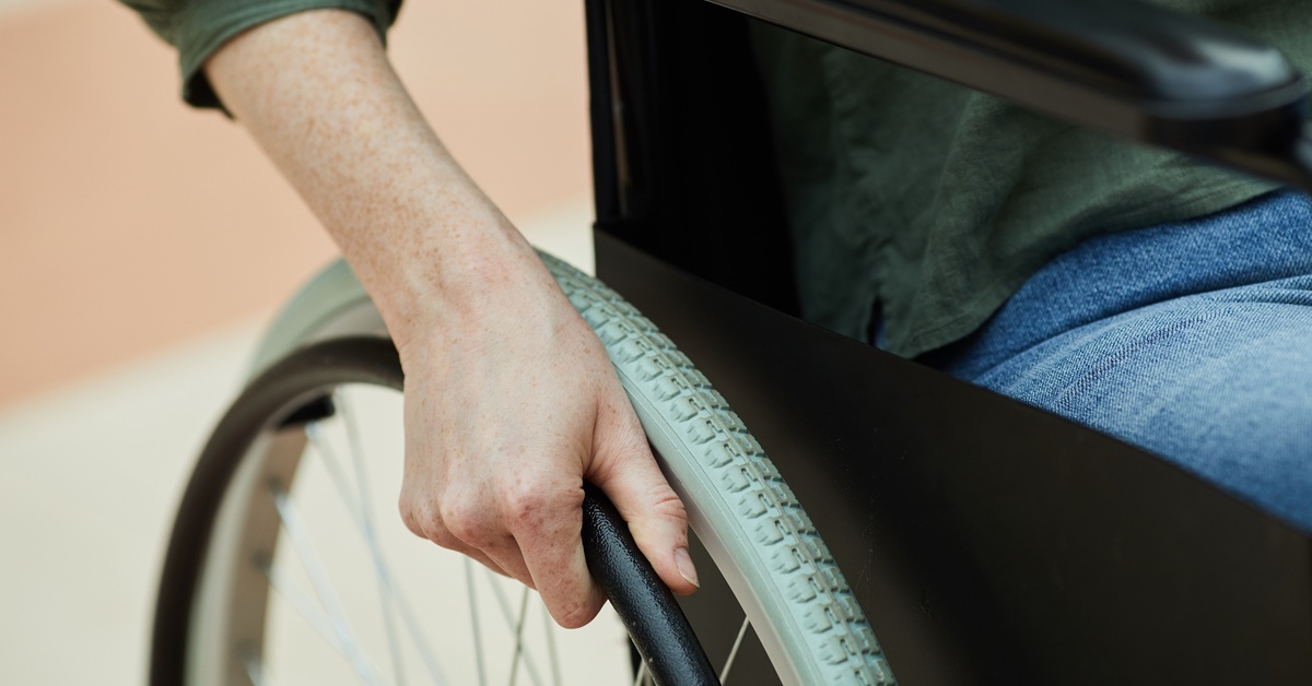 A woman sitting in a wheelchair with her hand on the tire to propel herself forward. She is wearing a green top. A woman sitting in a wheelchair with her hand on the tire to propel herself forward. She is wearing a green top.
