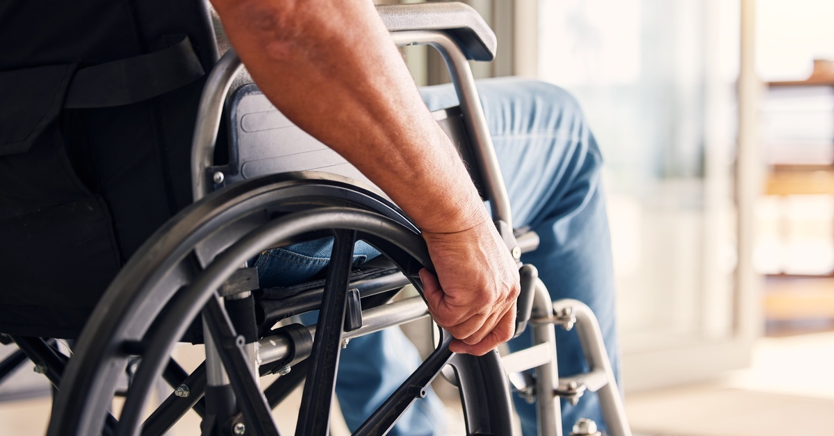 A close-up of a man sitting in a wheelchair. He is grasping the wheels of the chair to propel himself. A close-up of a man sitting in a wheelchair. He is grasping the wheels of the chair to propel himself.