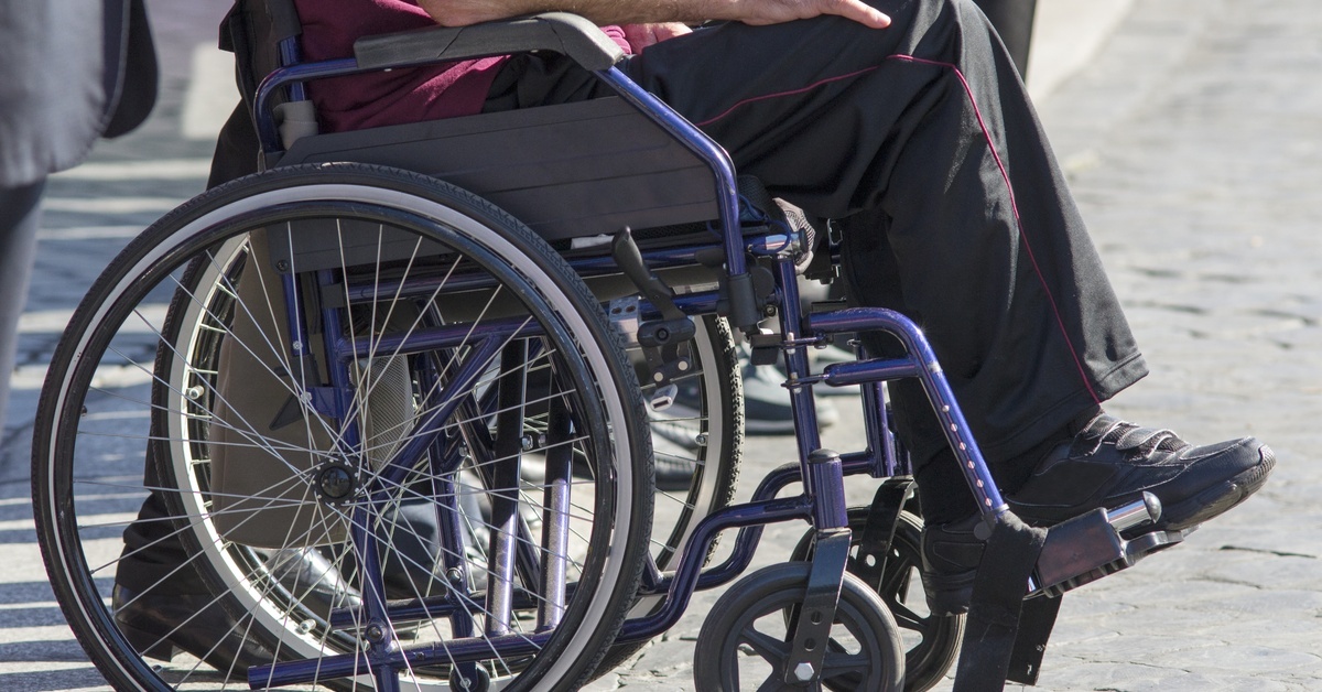 A man sitting in a wheelchair with his hands in his lap. The wheelchair has larger rear wheels and smaller front wheels.